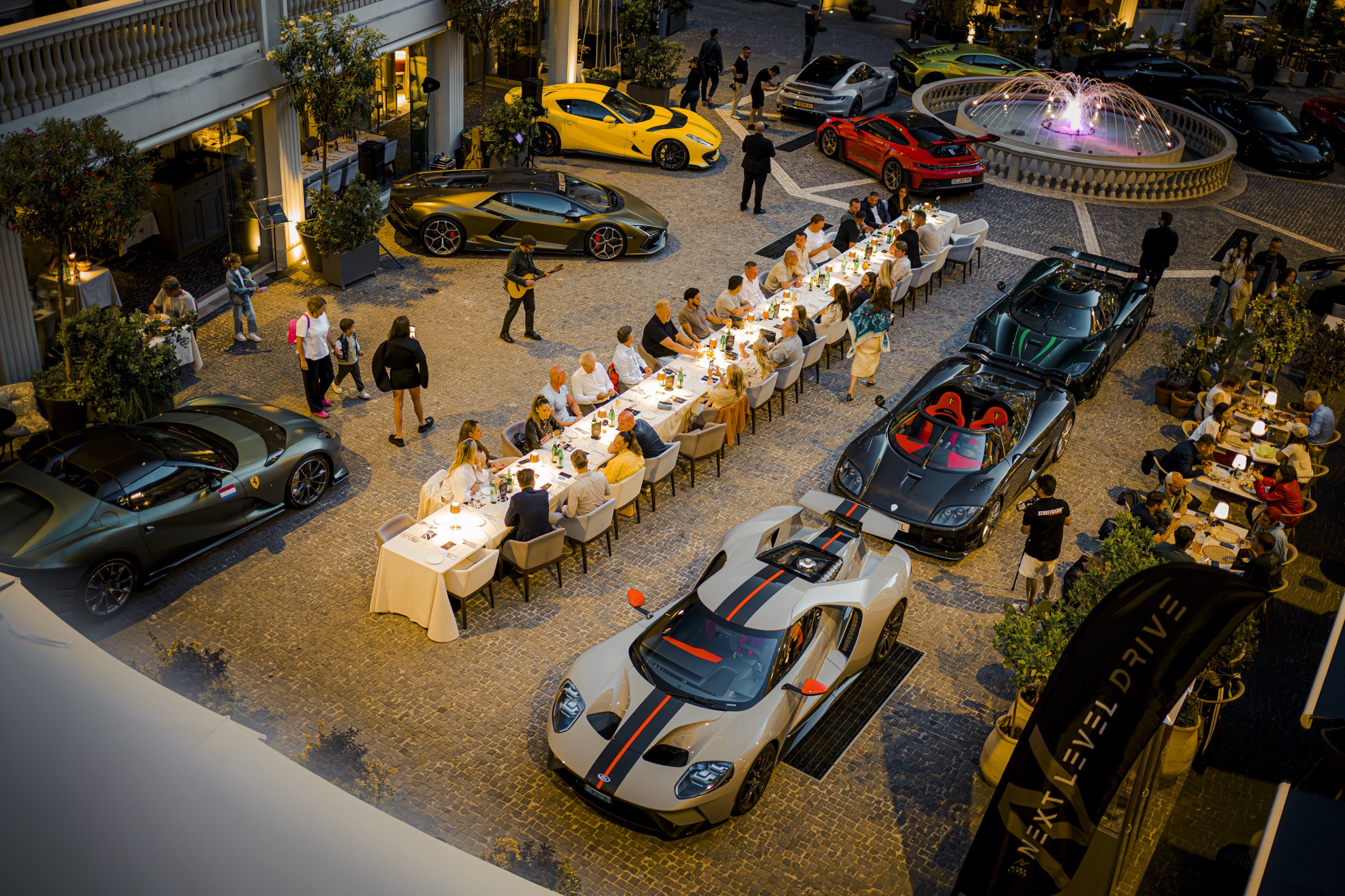 Luchtfoto van de clubtafel geflankeerd door supercars bij schemering.